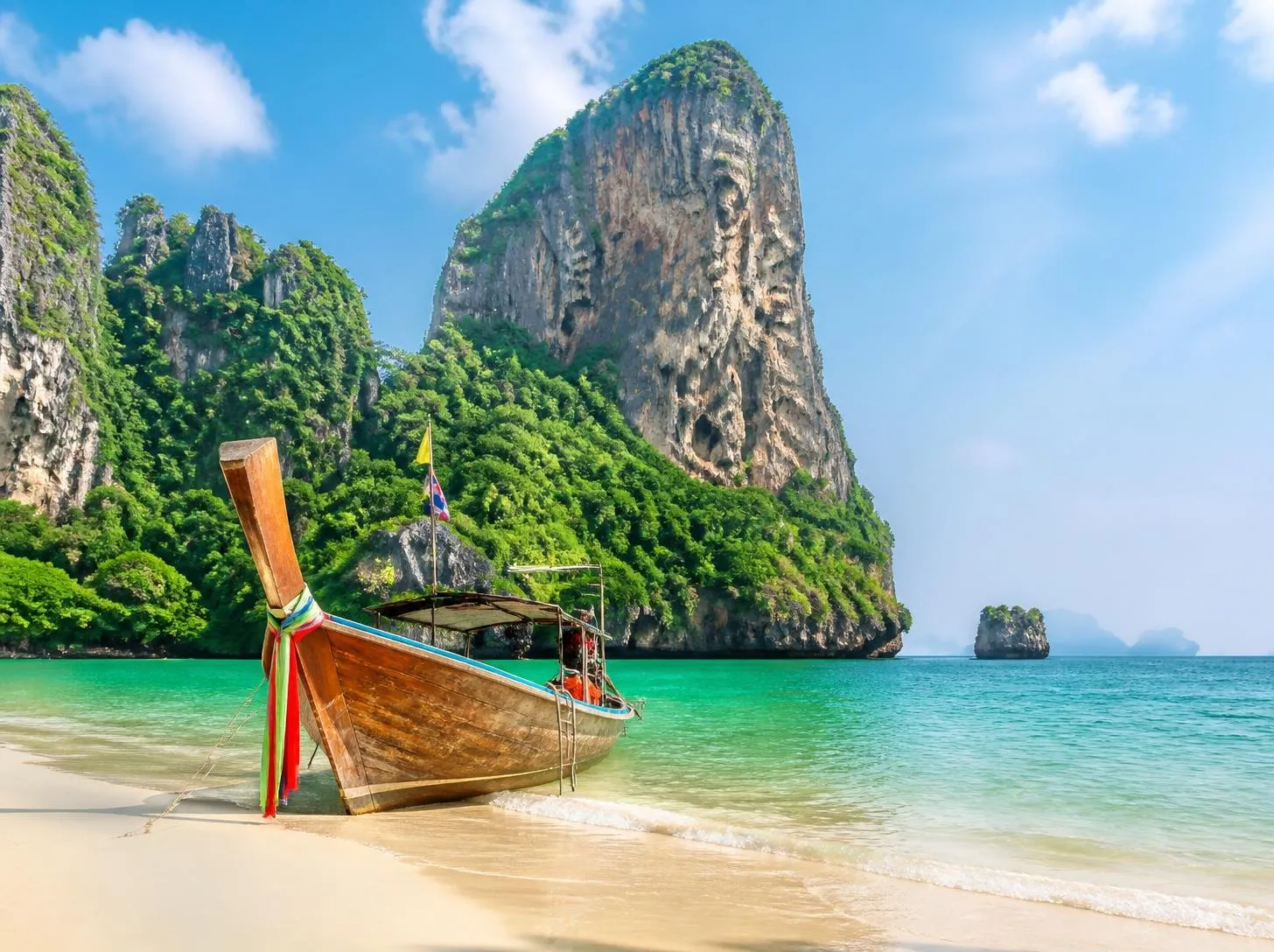 Longtail boat on a white-sand beach below limestone cliffs, Thailand